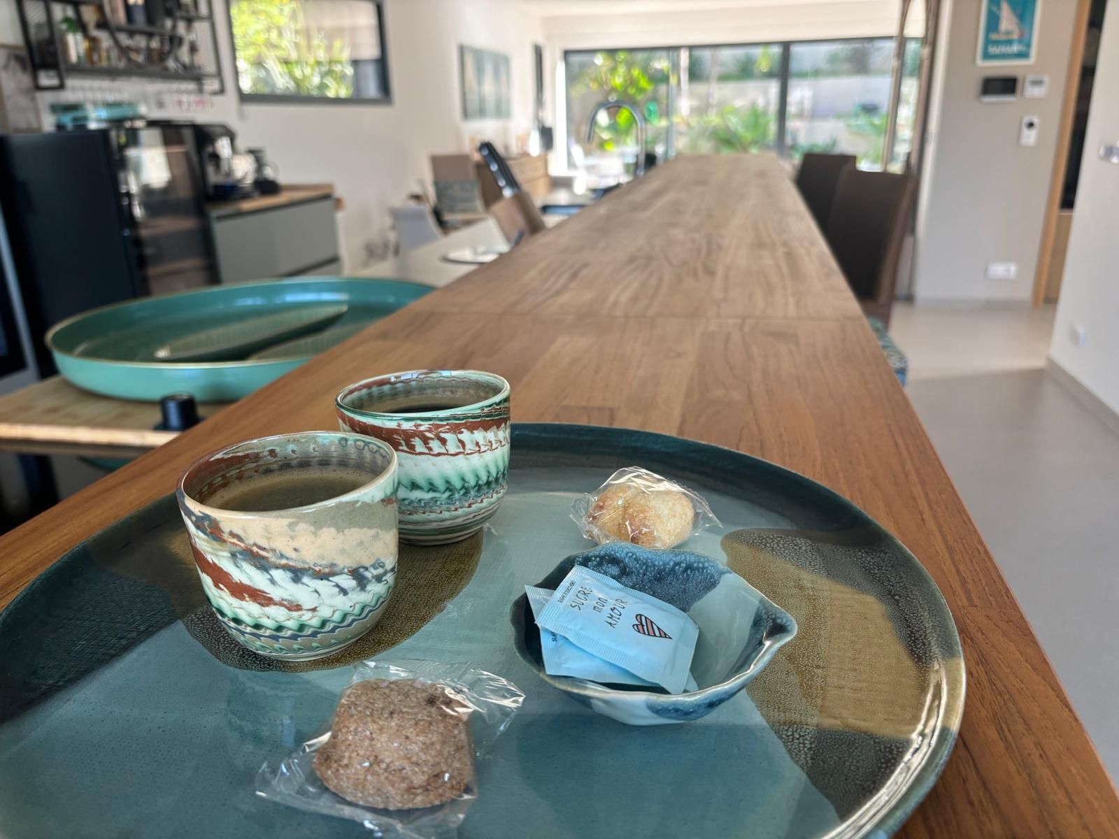 Deux tasses de café en céramique et des biscuits sur un plateau, posés sur un long comptoir en bois