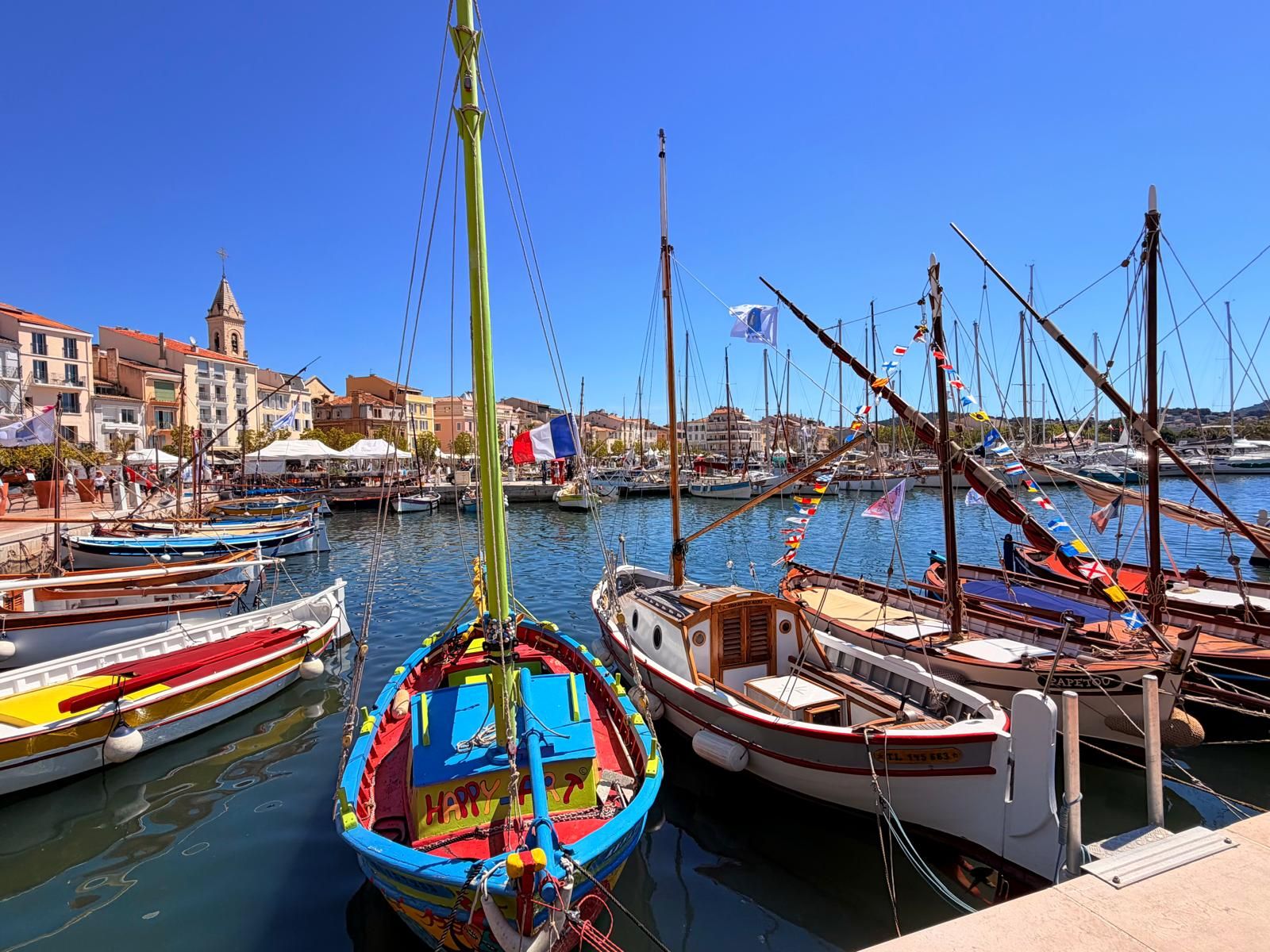 Pointus colorés amarrés dans le port de Sanary-sur-Mer, devant les façades et le clocher